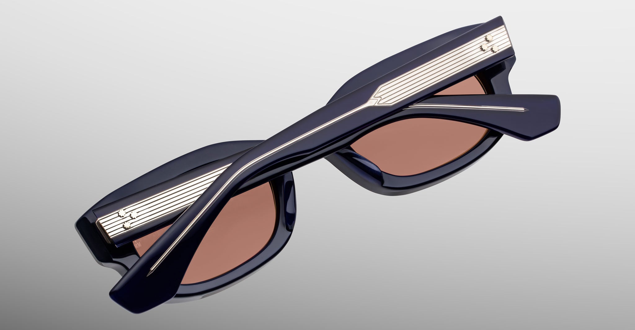 Jacques Marie Mage Whiskeyclone in Minuit sunglasses, deep navy blue acetate frame with rose-tinted lenses and intricately engraved silver-tone metal core temples featuring three-dot rivet detailing, shown folded in a close-up back view highlighting the sculpted frame and decorative hardware