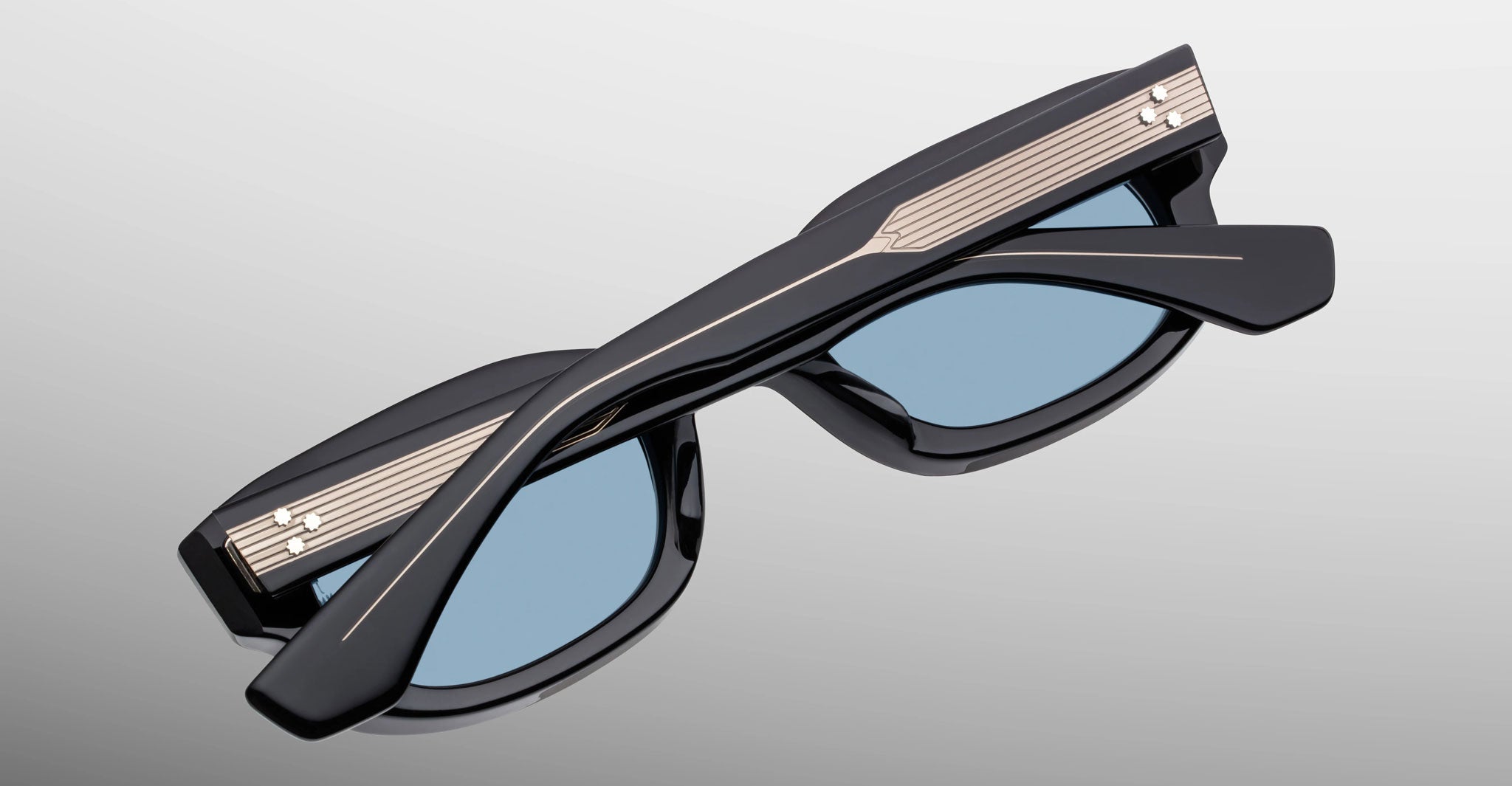 Jacques Marie Mage Whiskeyclone in Mystique sunglasses, dark charcoal acetate frame with light blue-tinted lenses and engraved silver-tone metal core temples featuring three-dot rivet detailing, shown folded in a close-up view highlighting the sculpted frame and decorative hardware