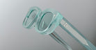 Close-up of Jacques Marie Mage Whiskeyclone eyeglass frames in translucent mint green with thick rims and two silver dots on the temples, set against a plain light grey background.