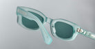 Close-up of Jacques Marie Mage Whiskeyclone sunglasses featuring translucent light blue frames and dark lenses, highlighting the frame and one arm against a plain grey background.