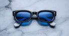 Jacques Marie Mage Whiskeyclone sunglasses, blue-tinted lenses, white arms, top view.