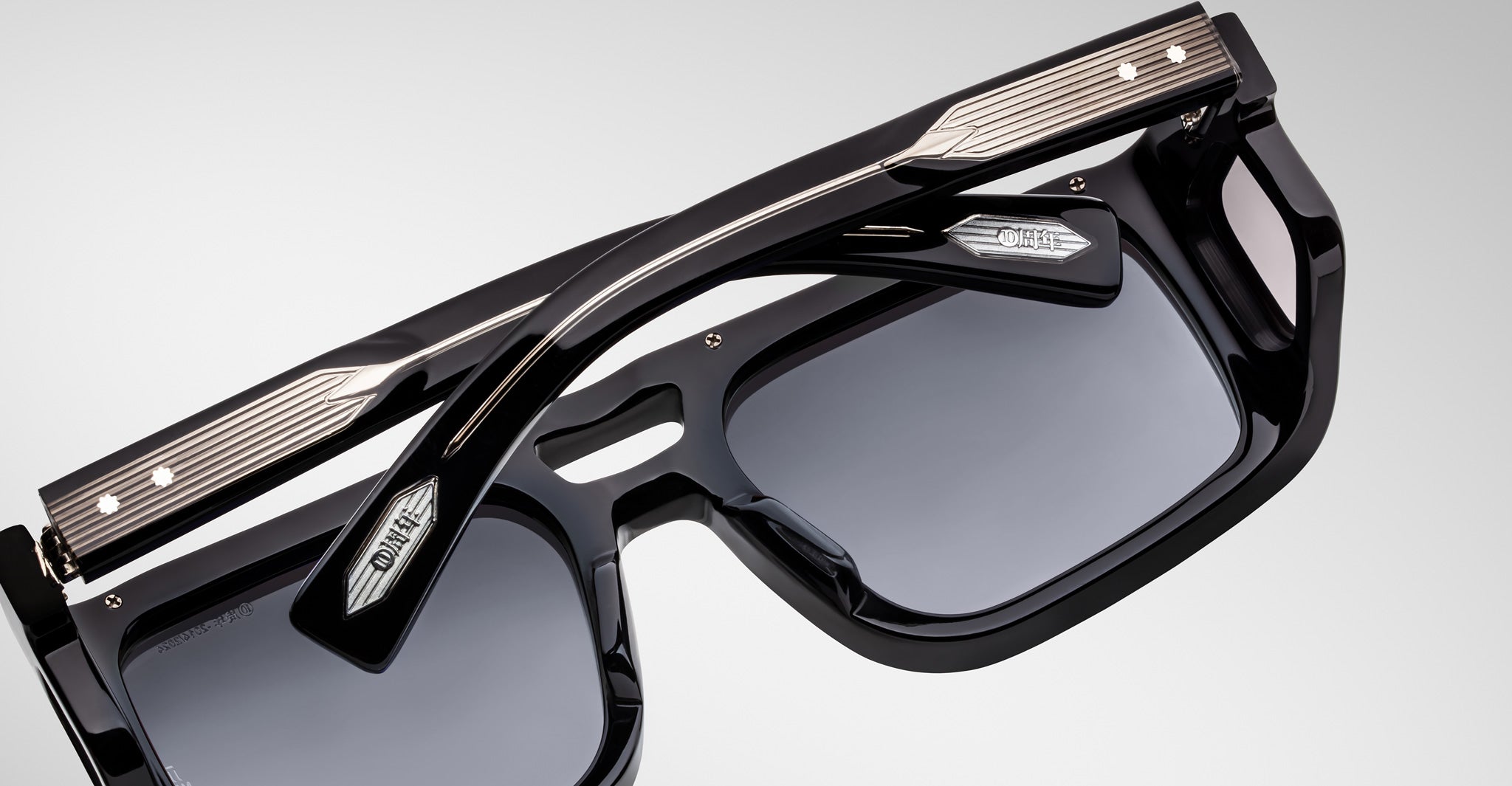 Close-up of Jacques Marie Mage Windsor sunglasses, black thick frames, silver accents, dark tinted lenses, front view.