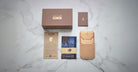 A Jacques Marie Mage Firehole River set—featuring a brown Yellowstone box, small brown booklet, tan leather pouch, card, and folded blue cloth with the Yellowstone bison logo—is displayed on white marble.