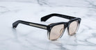 Jacques Marie Mage Yves sunglasses featuring black and translucent frames with light brown lenses, viewed from above.