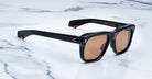 Jacques Marie Mage Yves black-framed sunglasses with brown lenses, shown from above.
