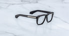 Jacques Marie Mage Yves in Obscure Black optical frame, rectangular matte black acetate frame with clear lenses, signature arrowhead rivets, and engraved metal core temples, angled side view