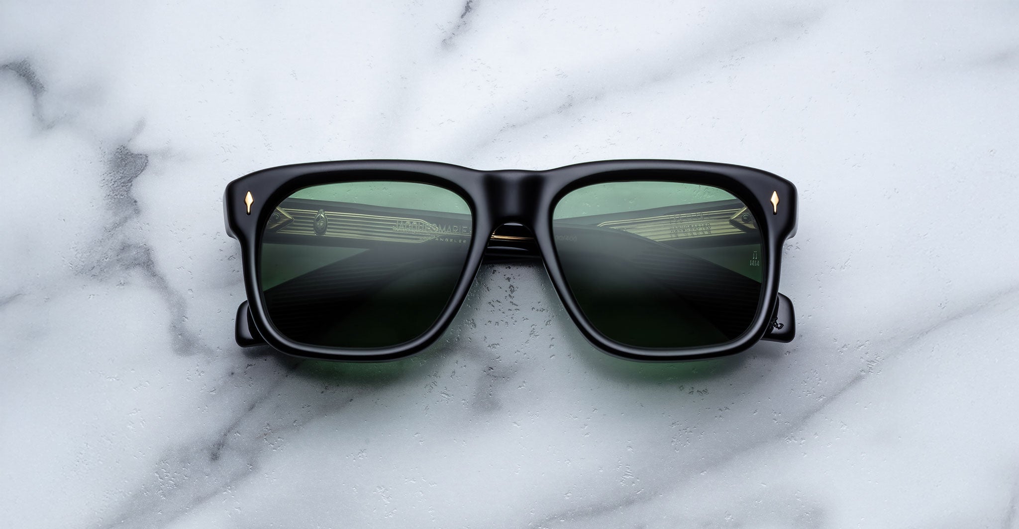 Jacques Marie Mage Yves sunglasses with green-tinted lenses, viewed from above, reflect a car dashboard.