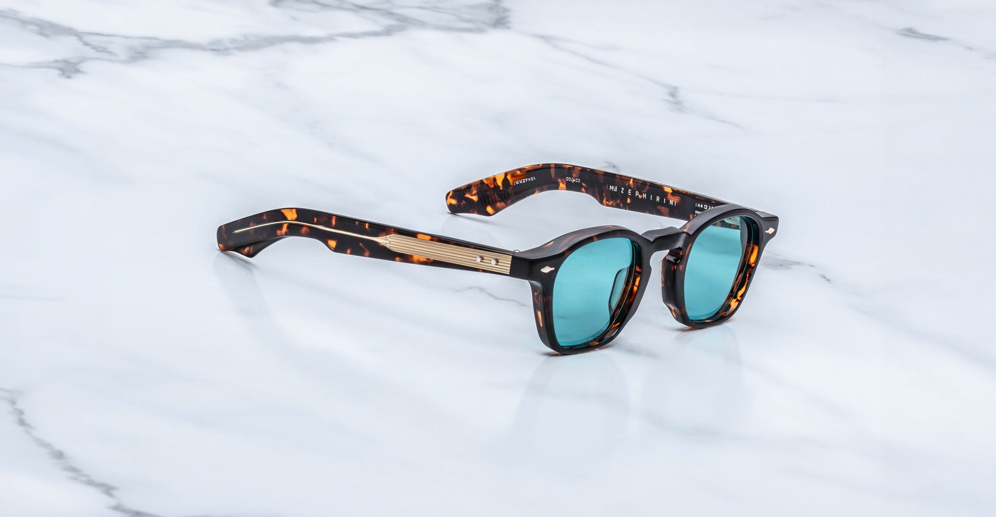 Jacques Marie Mage Zephirin sunglasses in Aegen with turquoise lenses, shown at an angle on a white marble surface.
