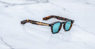 Jacques Marie Mage Zephirin sunglasses in Aegen with turquoise lenses, shown at an angle on a white marble surface.