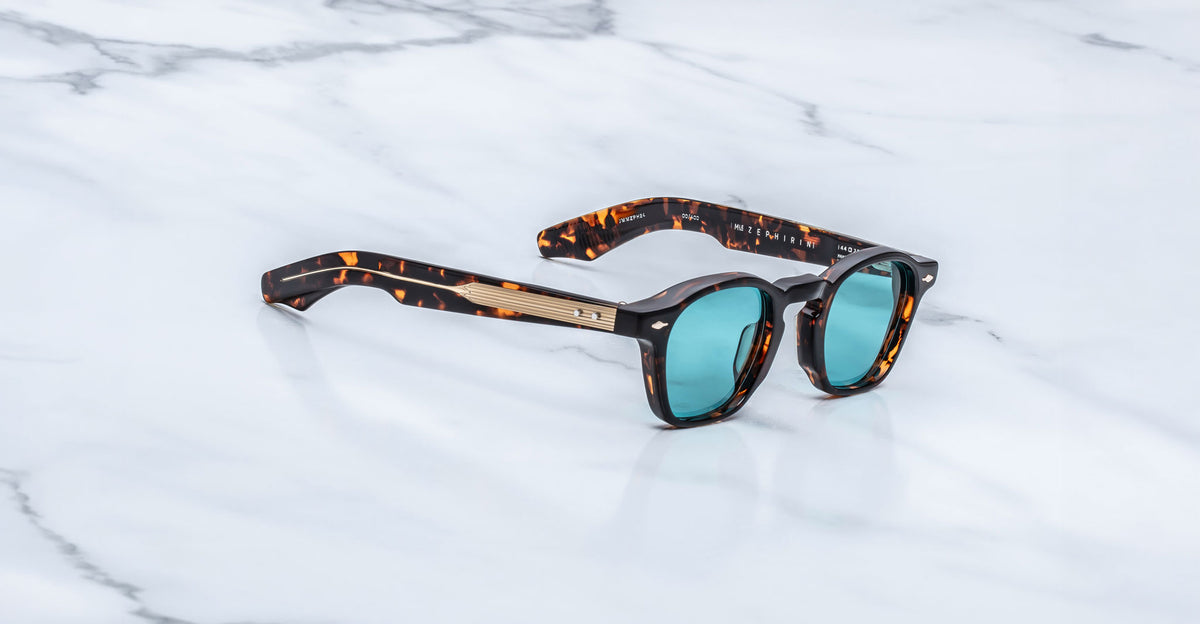 Jacques Marie Mage Zephirin sunglasses in Aegen with turquoise lenses, shown at an angle on a white marble surface.