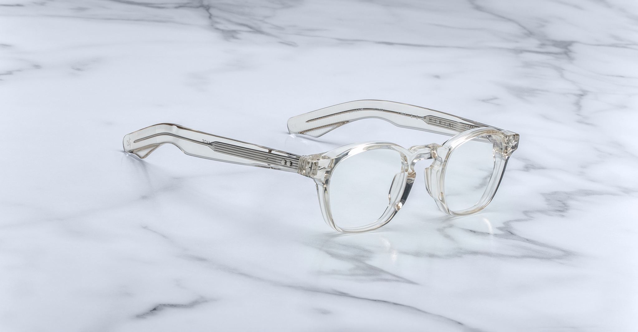 The Jacques Marie Mage Zephirin features handcrafted clear acetate with rectangular lenses and wide arms, displayed on white marble—a refined, limited edition spectacle from Jacques Marie Mage.