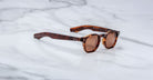 A handcrafted pair of Jacques Marie Mage Zephirin sunglasses featuring brown tortoiseshell acetate, round lenses, and thick frames, elegantly displayed on a white marble surface.