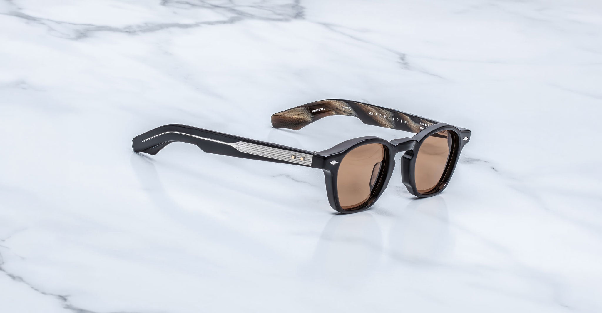Jacques Marie Mage Zephirin sunglasses in Brun, three-quarter view with dark brown acetate, warm brown lenses, and silver-tone accents on a white marble surface.