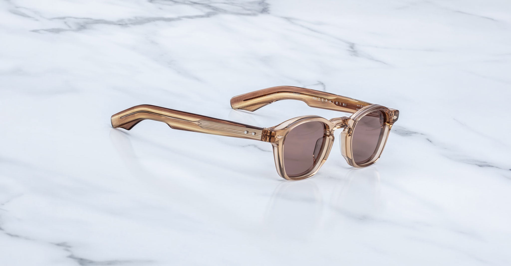 Jacques Marie Mage Zephirin sunglasses in Casliza, three-quarter view with translucent amber acetate and rose-tinted lenses on a white marble surface.