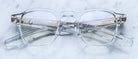 Jacques Marie Mage Zephirin spectacles by Jacques Marie Mage feature clear handcrafted acetate frames, rectangular lenses, and metal hinges. Temples crossed on a white marble surface—a subtle nod to limited edition eyewear.
