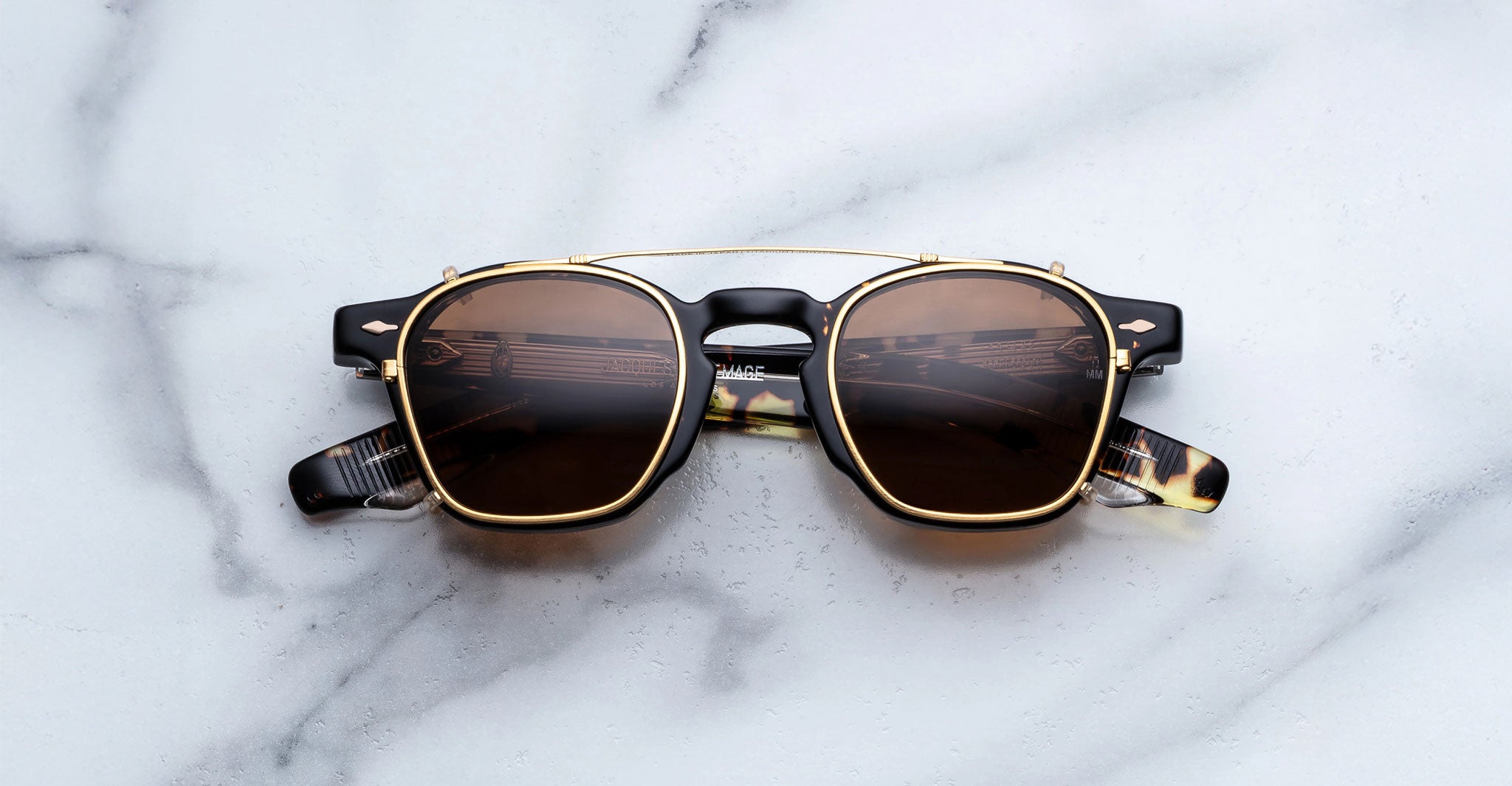 Jacques Marie Mage Zephirin Clip On 2 sunglasses with gold and black frames, viewed from above.