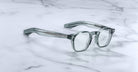 The Jacques Marie Mage Zephirin, handcrafted acetate spectacles with round lenses and thick arms, rest on a white marble surface—a refined piece from the exclusive Jacques Marie Mage collection.