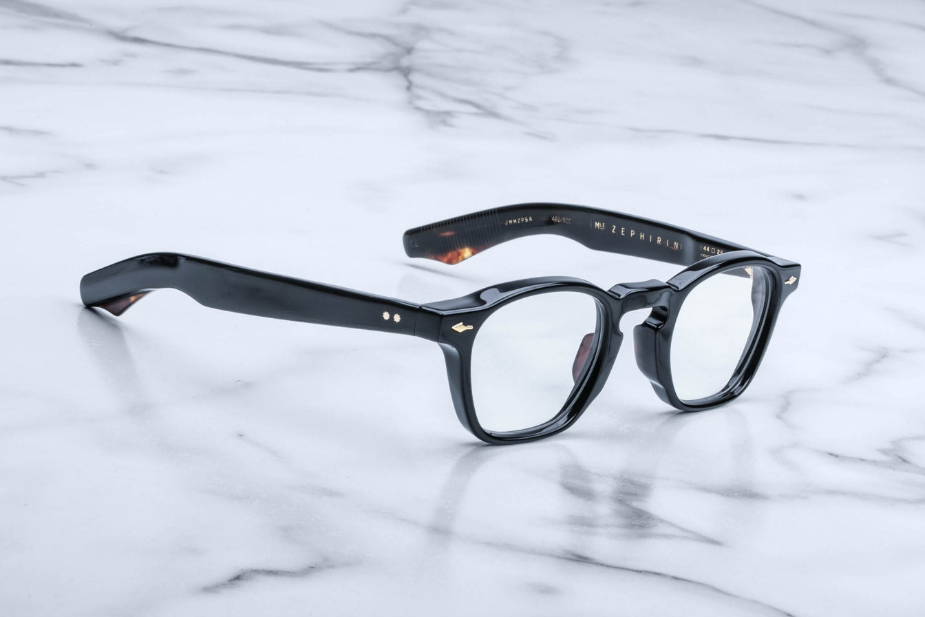 A pair of Jacques Marie Mage Zephirin rectangular eyeglasses with clear lenses, handcrafted in acetate, rests elegantly on a white marble surface.