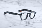A pair of Jacques Marie Mage Zephirin rectangular eyeglasses with clear lenses, handcrafted in acetate, rests elegantly on a white marble surface.