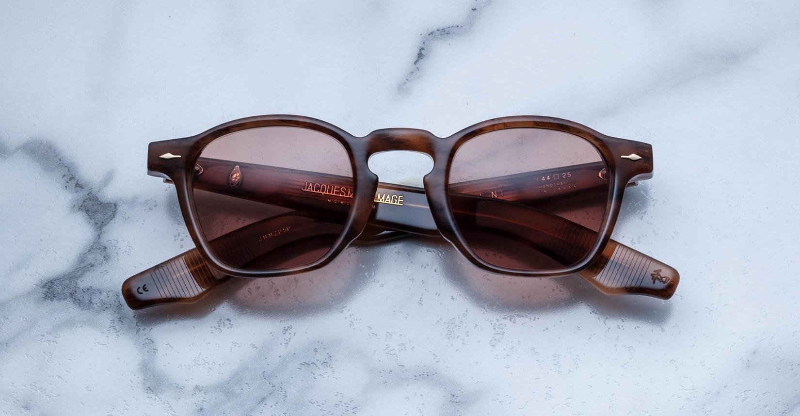 A pair of Jacques Marie Mage Zephirin brown square-framed sunglasses with tinted lenses rests on white marble, highlighting the sophistication of this limited edition eyewear.