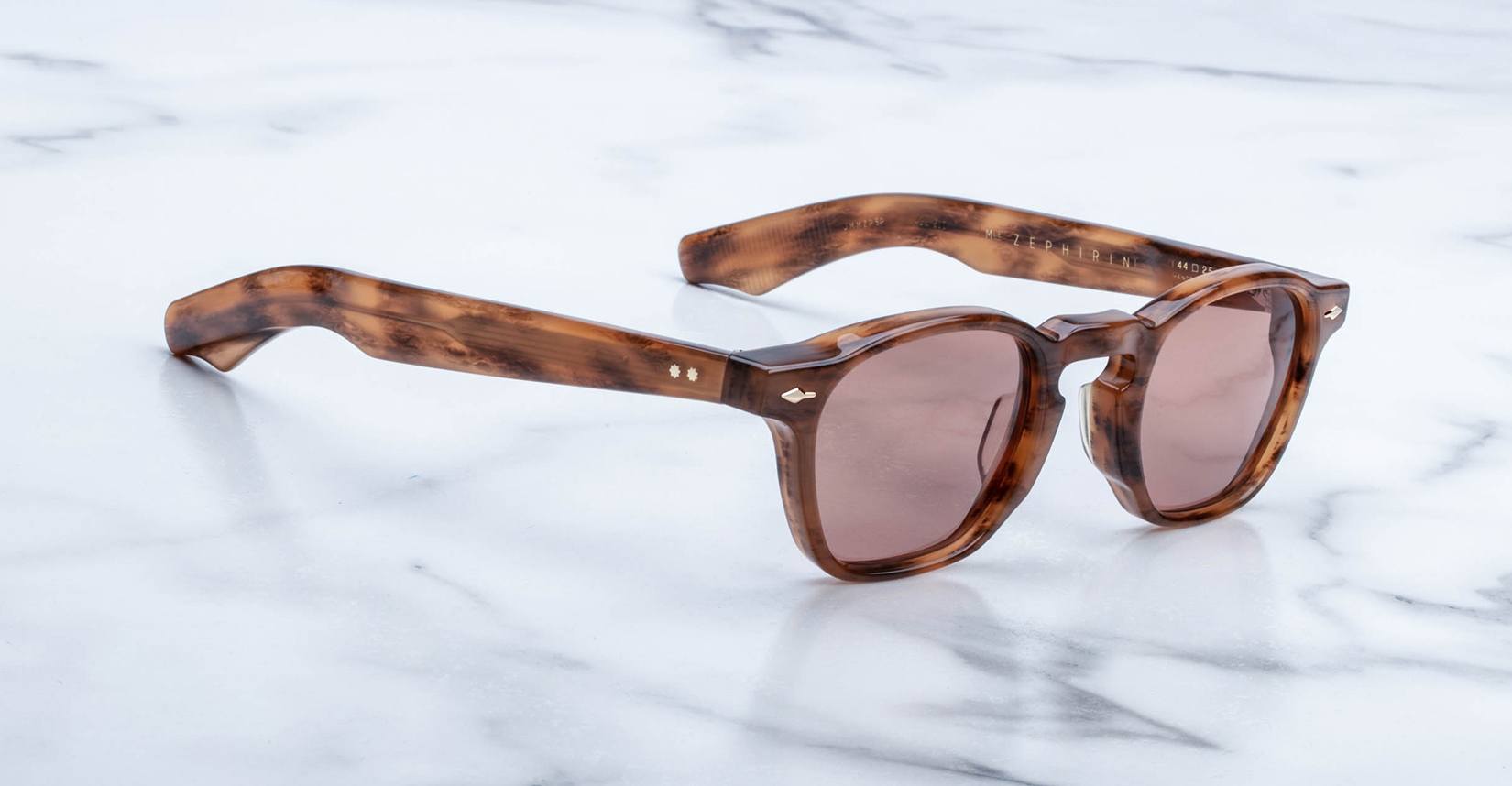 The limited edition Jacques Marie Mage Zephirin sunglasses feature round brown lenses and thick tortoiseshell acetate frames, handcrafted by Jacques Marie Mage and elegantly displayed on a white marble surface.