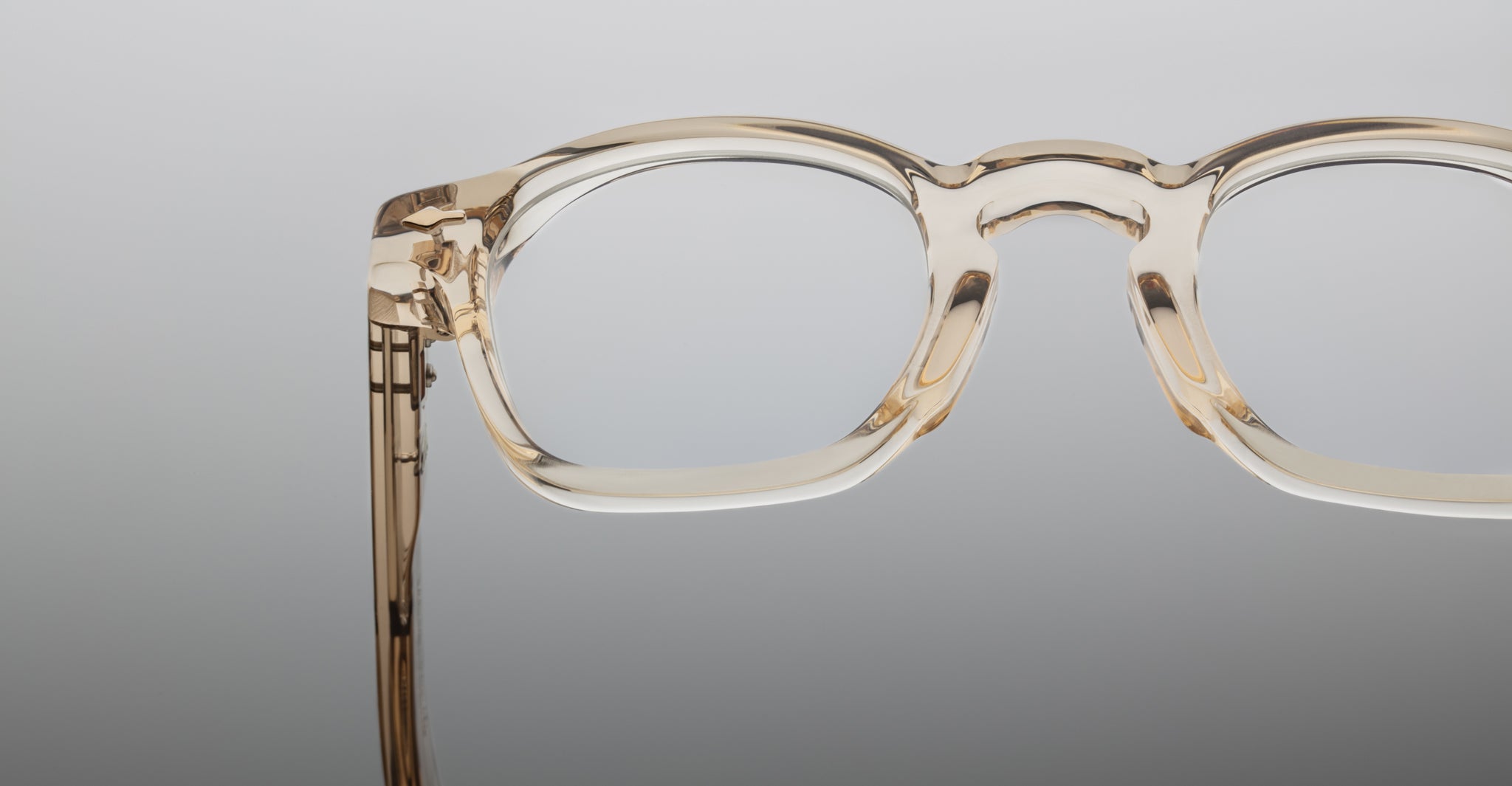 Close-up of the clear, thick-rimmed Jacques Marie Mage Zephirin frames in transparent beige, highlighting handcrafted acetate detail against a plain background.