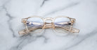 Jacques Marie Mage Zephirin eyeglasses by Jacques Marie Mage, featuring round lenses and transparent frames, are folded and placed on a white marble surface.