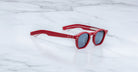 Limited edition Jacques Marie Mage Zephirin sunglasses with red frames and dark lenses rest stylishly on a white marble surface.