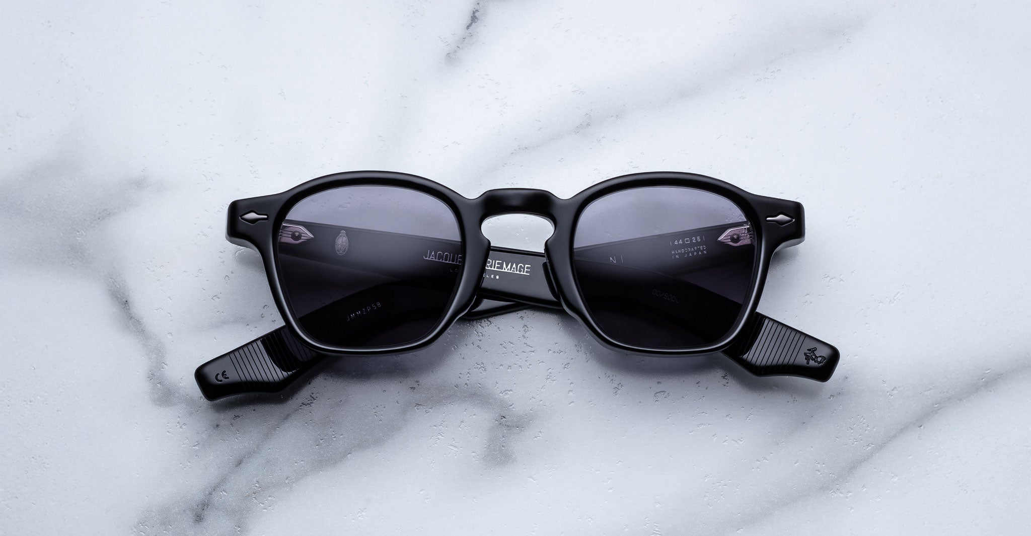 The Jacques Marie Mage Zephirin sunglasses, limited edition with black frames and dark lenses, are showcased on a white marble surface.