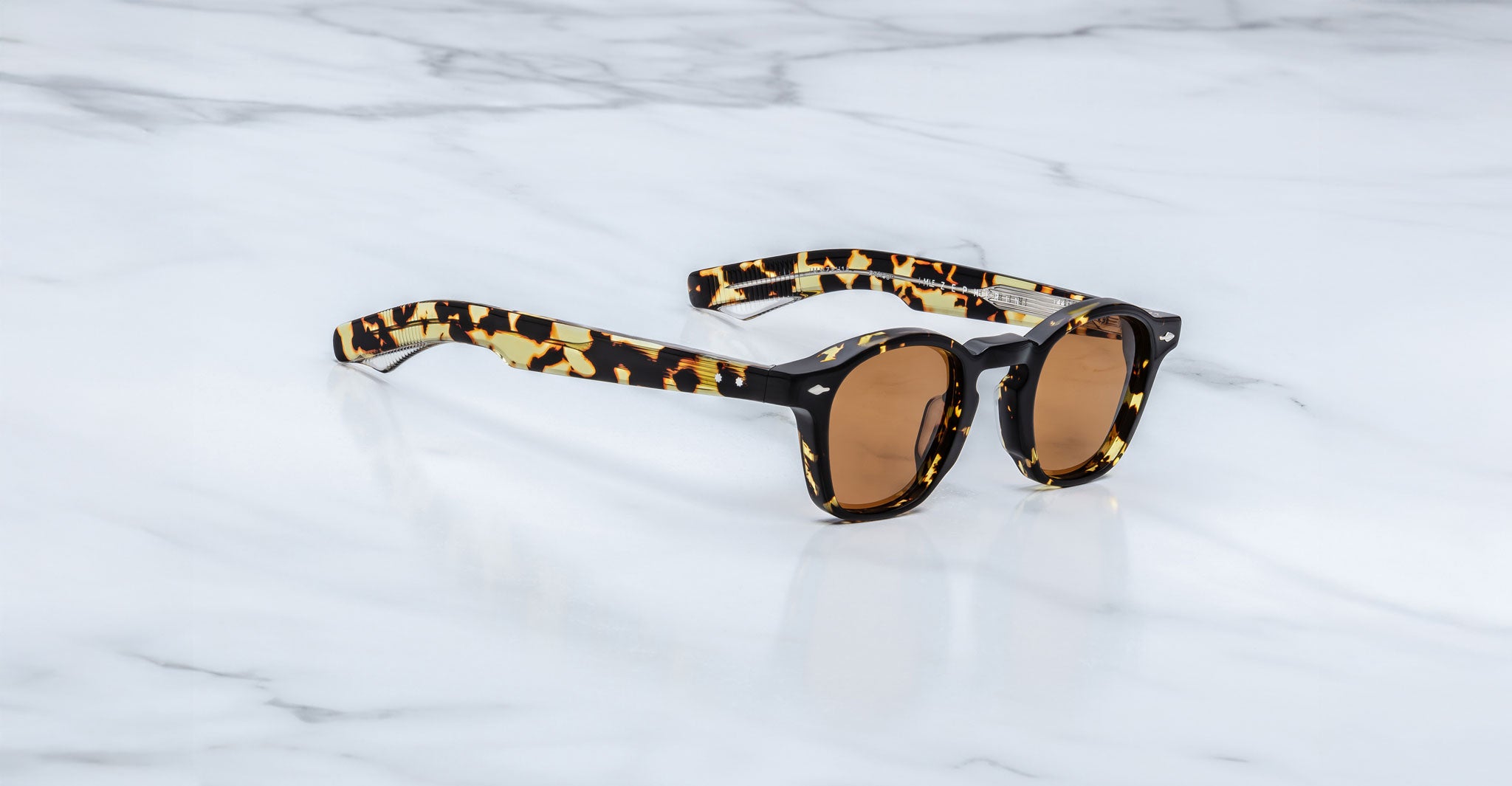 Jacques Marie Mage Zephirin sunglasses by Jacques Marie Mage, featuring tortoiseshell frames and brown lenses, rest on a white marble surface and highlight the exclusive charm of limited edition eyewear.