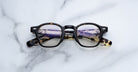 Jacques Marie Mage Zephirin black and tortoiseshell round handcrafted acetate eyeglasses with clear lenses by Jacques Marie Mage are placed closed on a white marble surface.