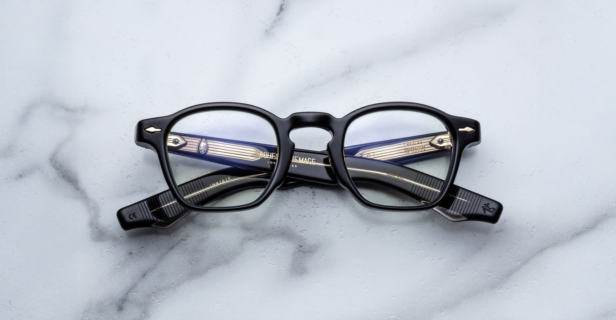 Jacques Marie Mage Zephirin black-framed eyeglasses, handcrafted from acetate with the brand name visible on the arms, elegantly displayed on a white marble surface.