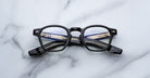 Jacques Marie Mage Zephirin black-framed eyeglasses, handcrafted from acetate with the brand name visible on the arms, elegantly displayed on a white marble surface.