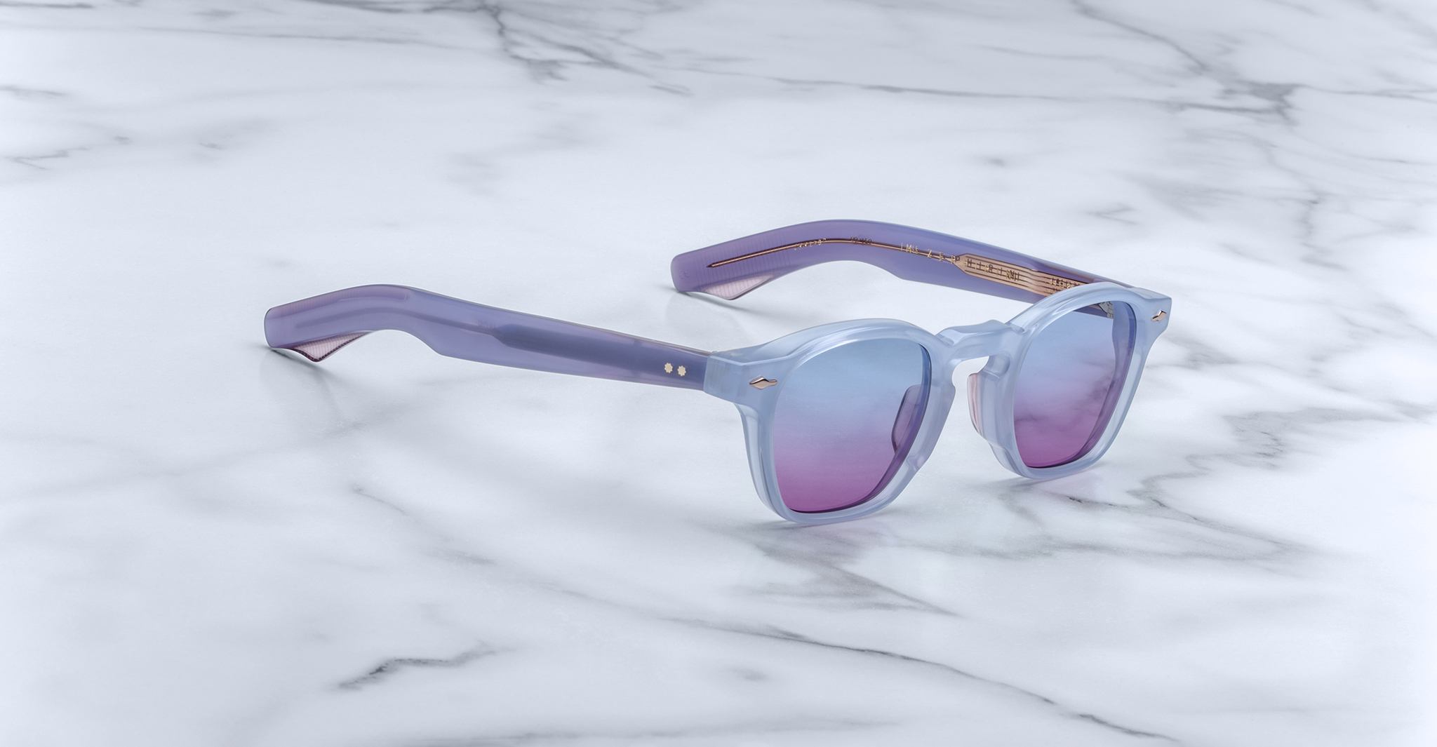 Jacques Marie Mage Zephirin sunglasses in light purple with tinted lenses are displayed on white marble—a striking, limited edition eyewear piece by Jacques Marie Mage.