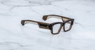 Jacques Marie Mage Zimmerman optical glasses in London brown acetate with bold rectangular frame, clear lenses, and wide temples with signature metal core detail, angled view