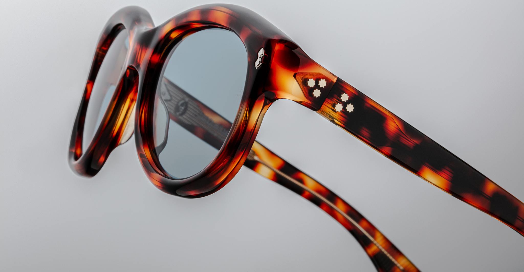 Jacques Marie Mage Jennie tortoiseshell sunglasses, close-up view, featuring round lenses and white flower accents on the frame.