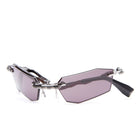 Futuristic sunglasses with angular, asymmetrical purple lenses, exposed metallic hinges, and black temples, displayed on a white background.