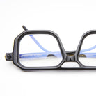 Close-up of KUBORAUM P8 eyeglasses, featuring black geometric frames and blue temples, angled for a detailed product view.