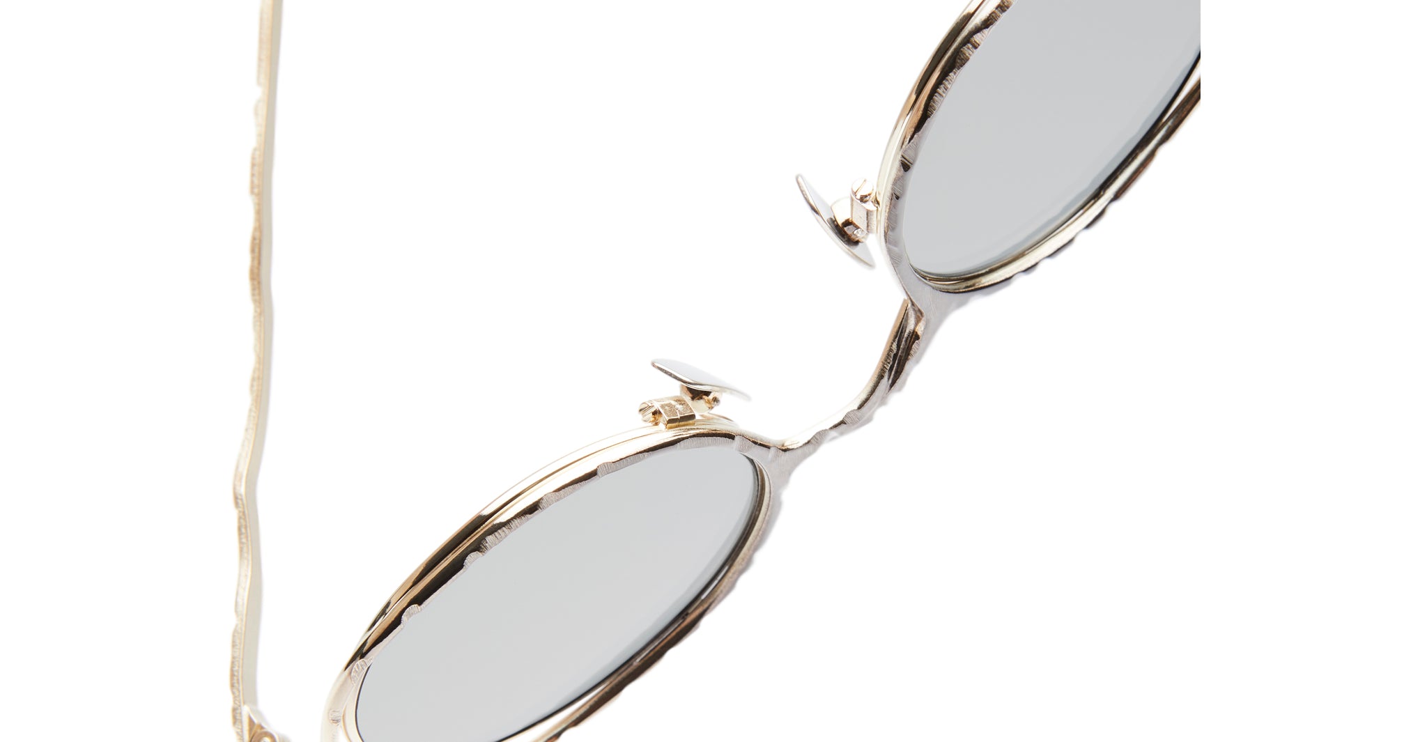 Close-up of the Kuboraum H11 oval sunglasses featuring gold metal frames and grey lenses, partially shown against a white background.