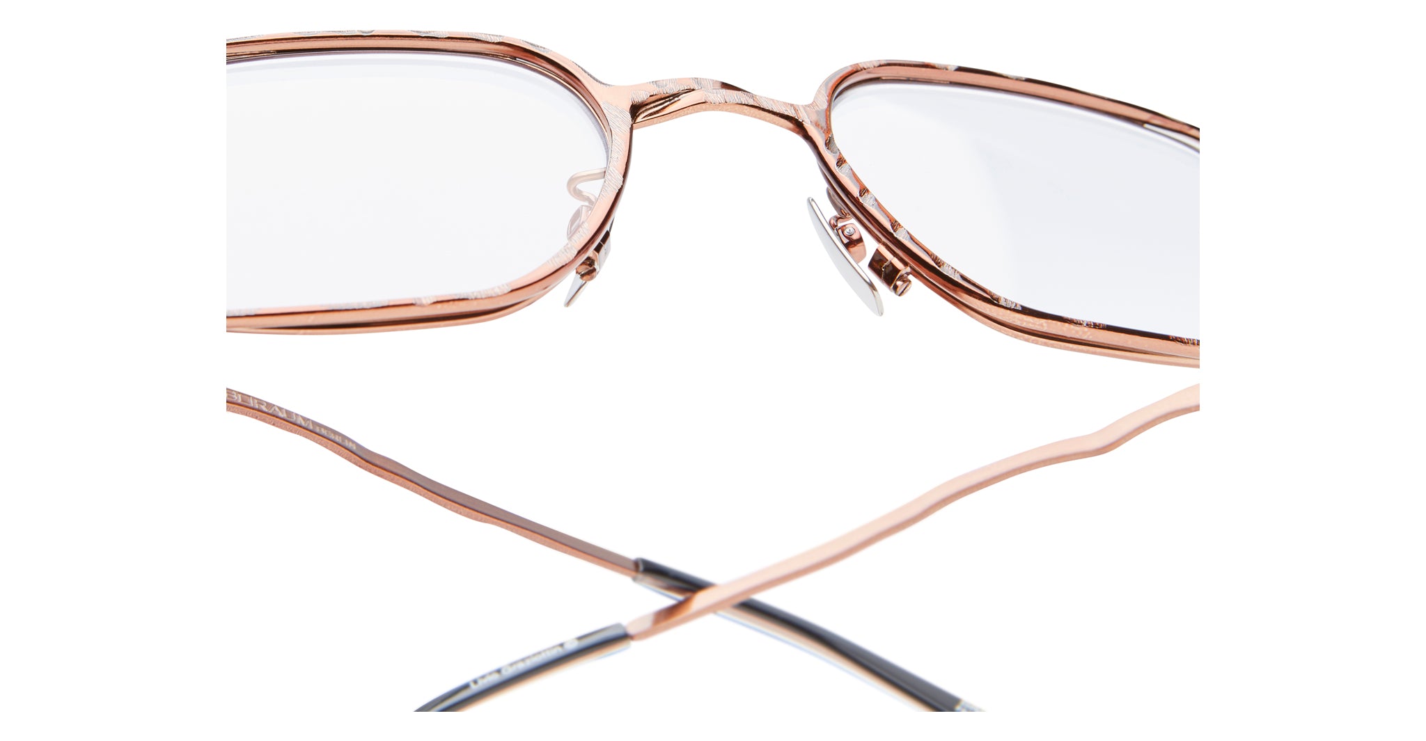 Close-up view of Kuboraum H22 eyeglasses in rose gold metal with clear lenses, adjustable nose pads, and partially visible temple arms crossed at the bottom against a white background.