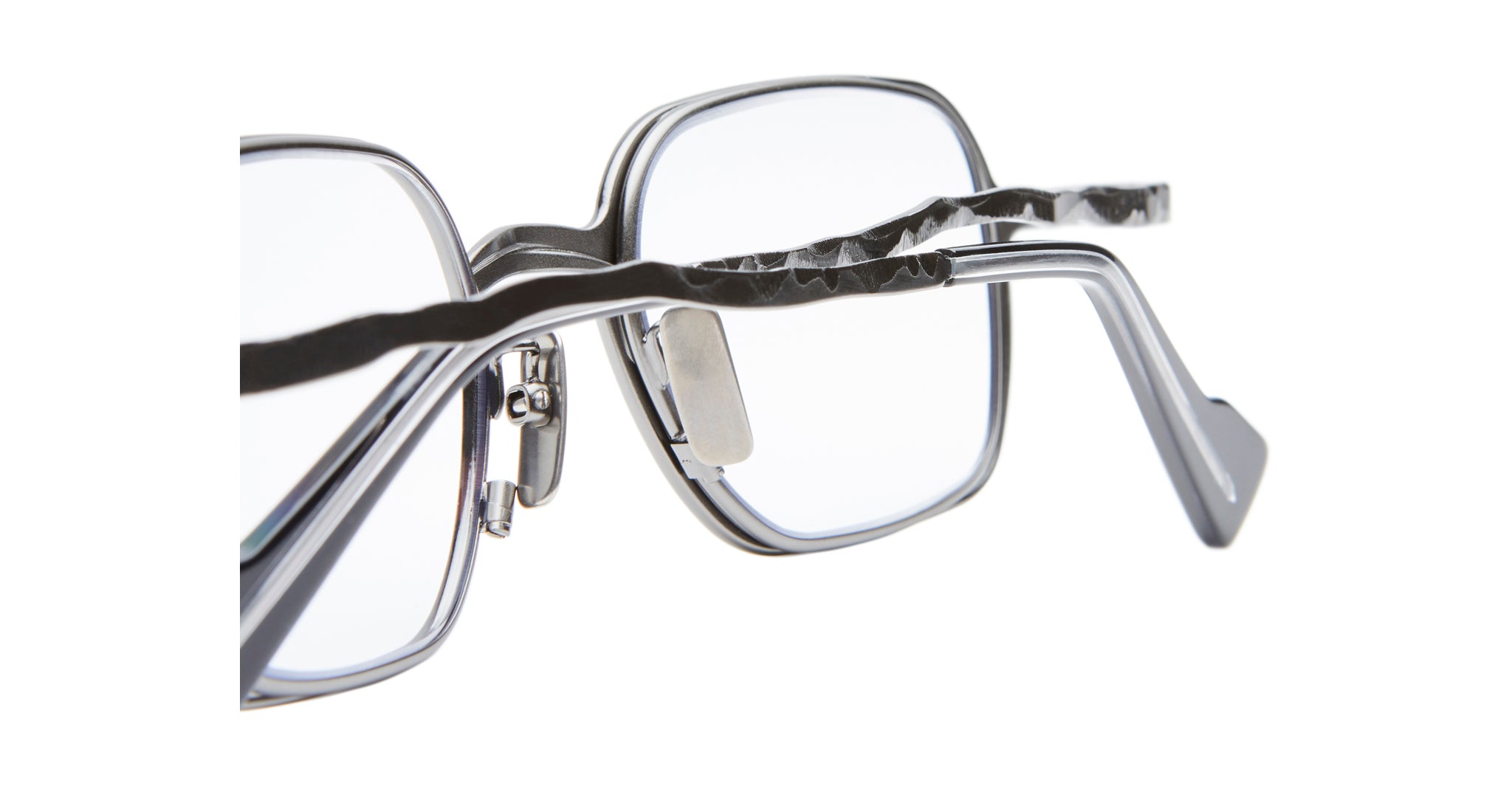 Close-up of Kuboraum H22 eyeglasses featuring rectangular lenses and distinctive wavy metal arms. The image focuses on the textured temple design and clear lenses against a white background.