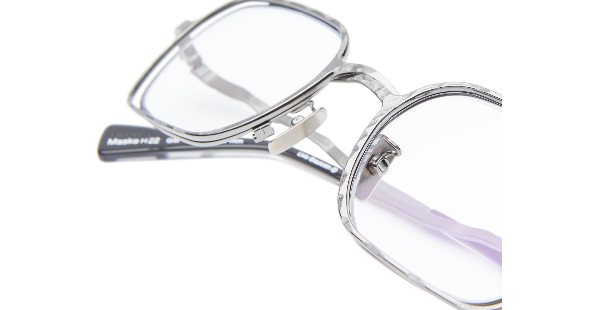 Close-up view of Kuboraum H22 square, silver-gray eyeglass frames with clear lenses, highlighting their detailed texture and a portion of the dark-colored temple arms.