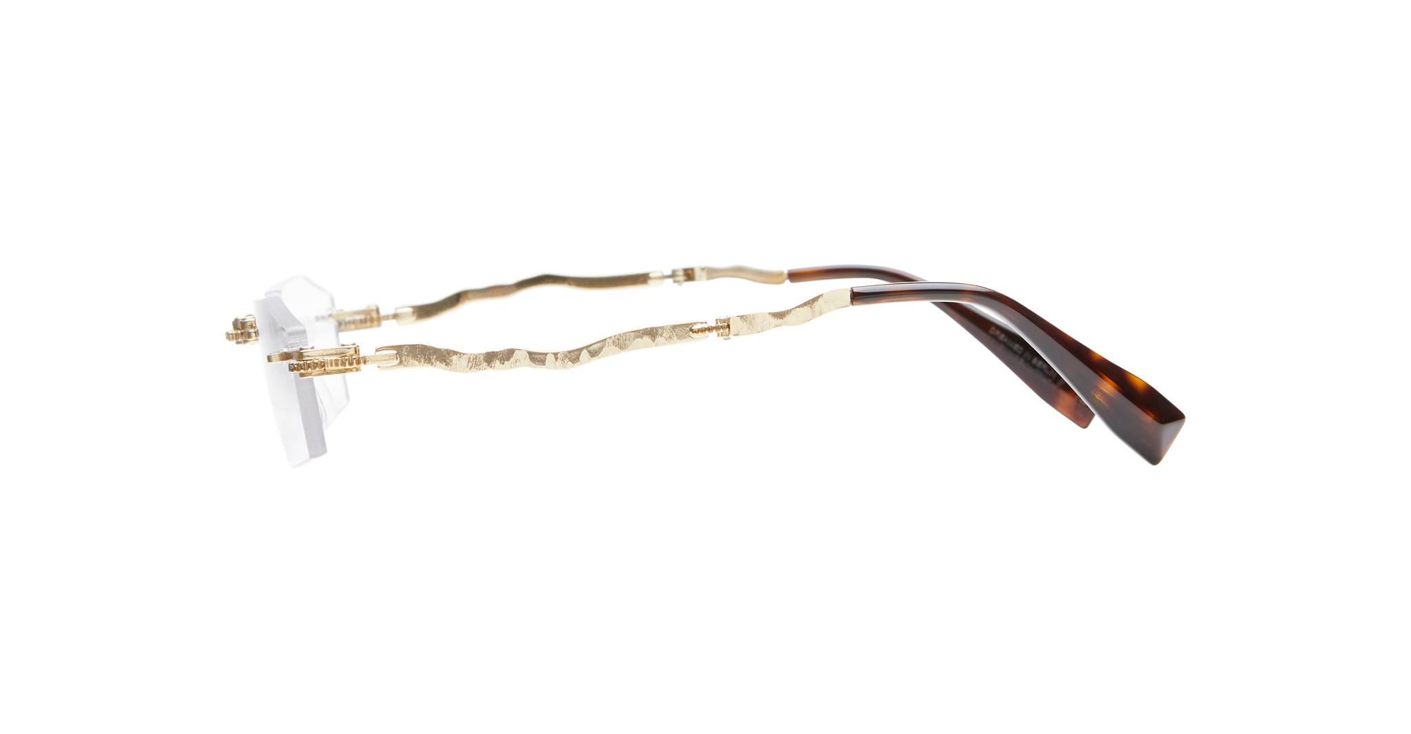 Side view of Kuboraum H40 rimless eyeglasses featuring gold, wavy metal arms and tortoiseshell-patterned temple tips, displayed on a white background.