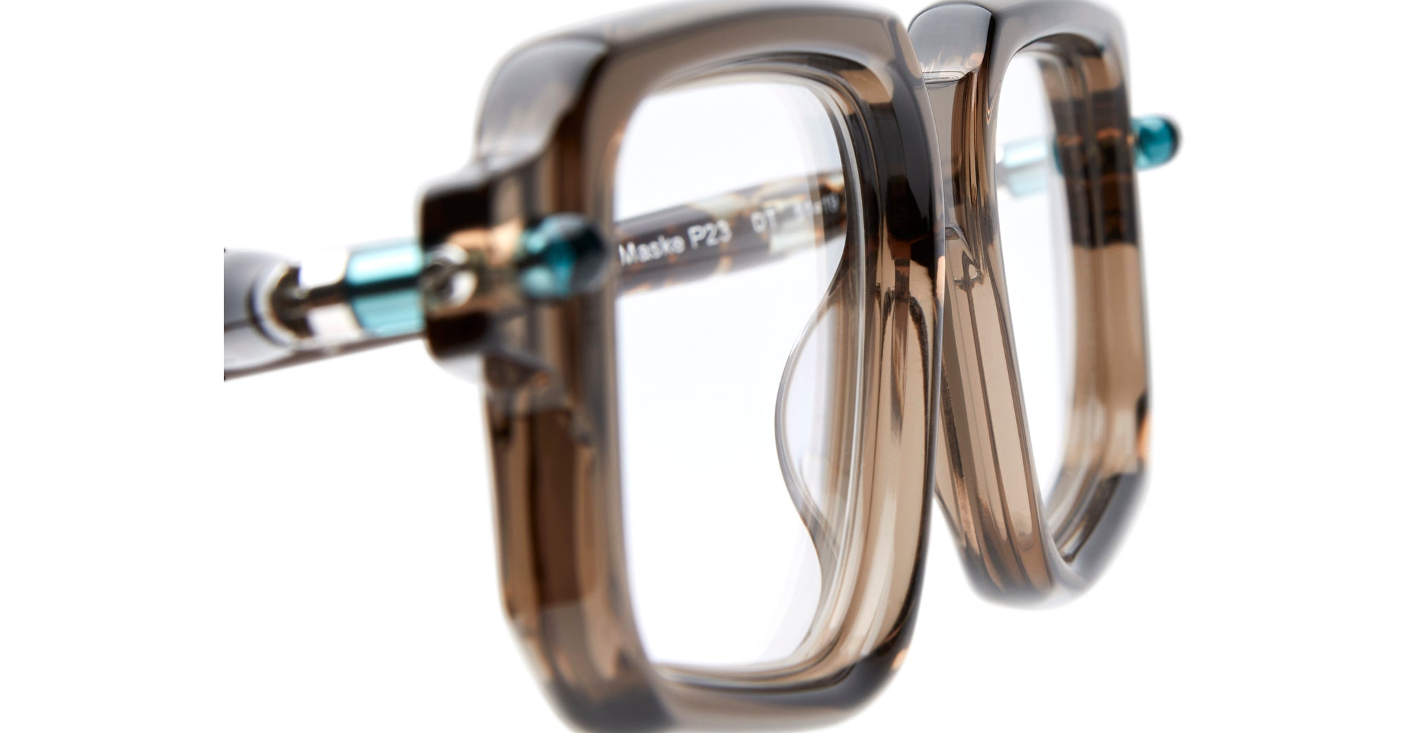 Close-up of the Kuboraum P23: oversized, thick, square eyeglass frames crafted from translucent brown plastic, shown at an angle with clear lenses and visible metal hinges.