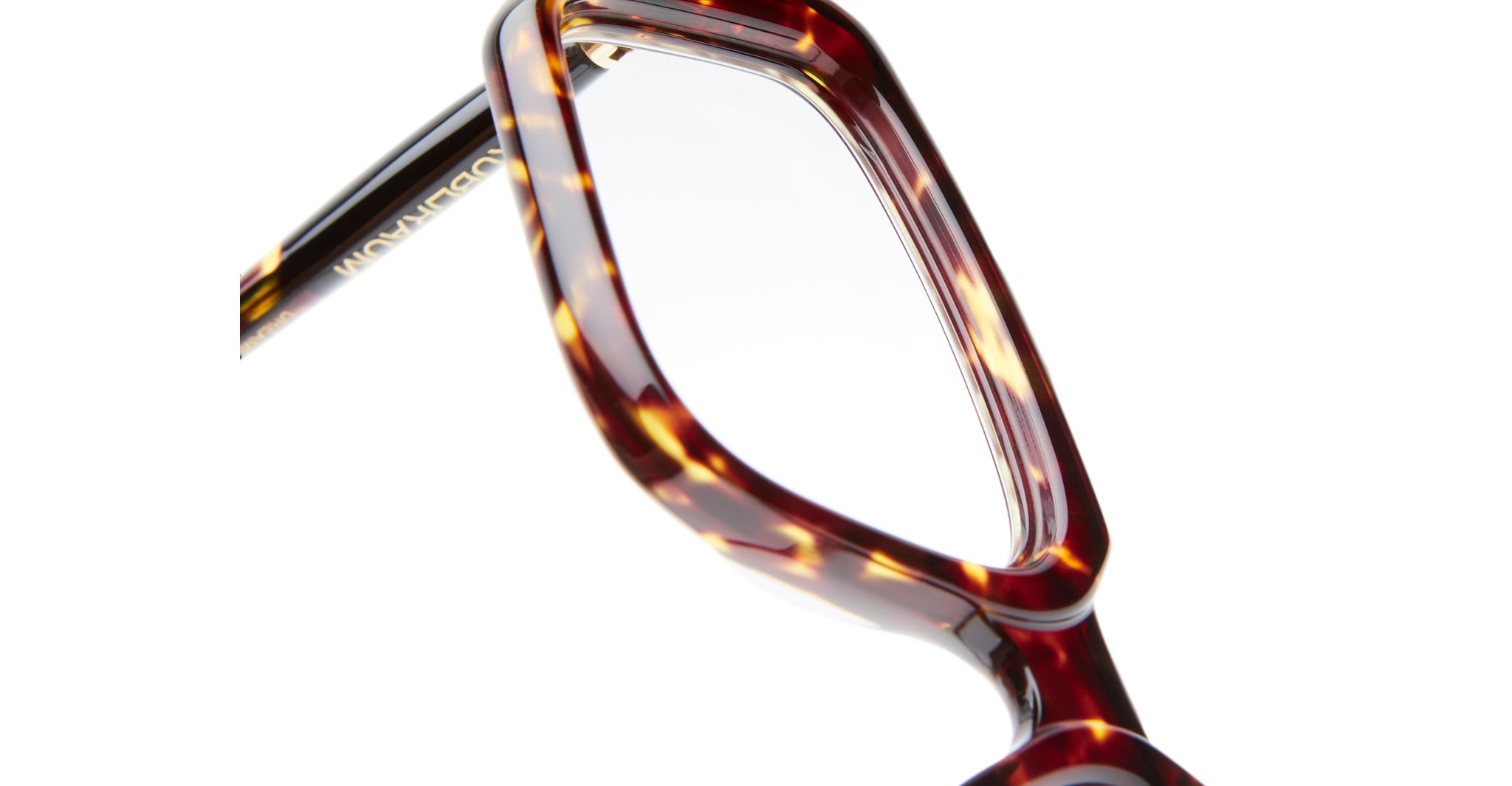 Close-up of the corner of Kuboraum P23 eyeglasses featuring a brown and yellow tortoiseshell pattern, set against a white background.