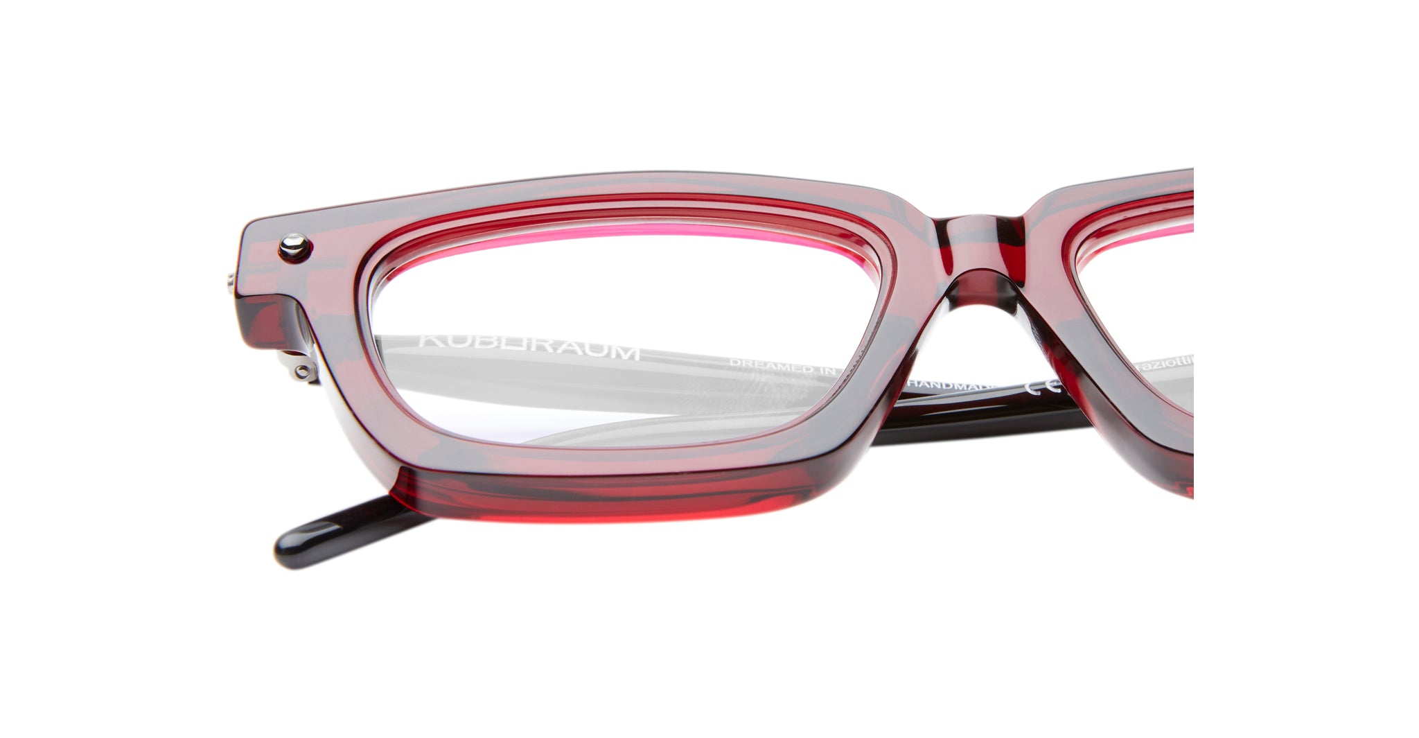 Close-up of Kuboraum P25 eyeglasses with thick, translucent pink and red frames, highlighting the upper half of the lenses and part of the temple arm against a white background.