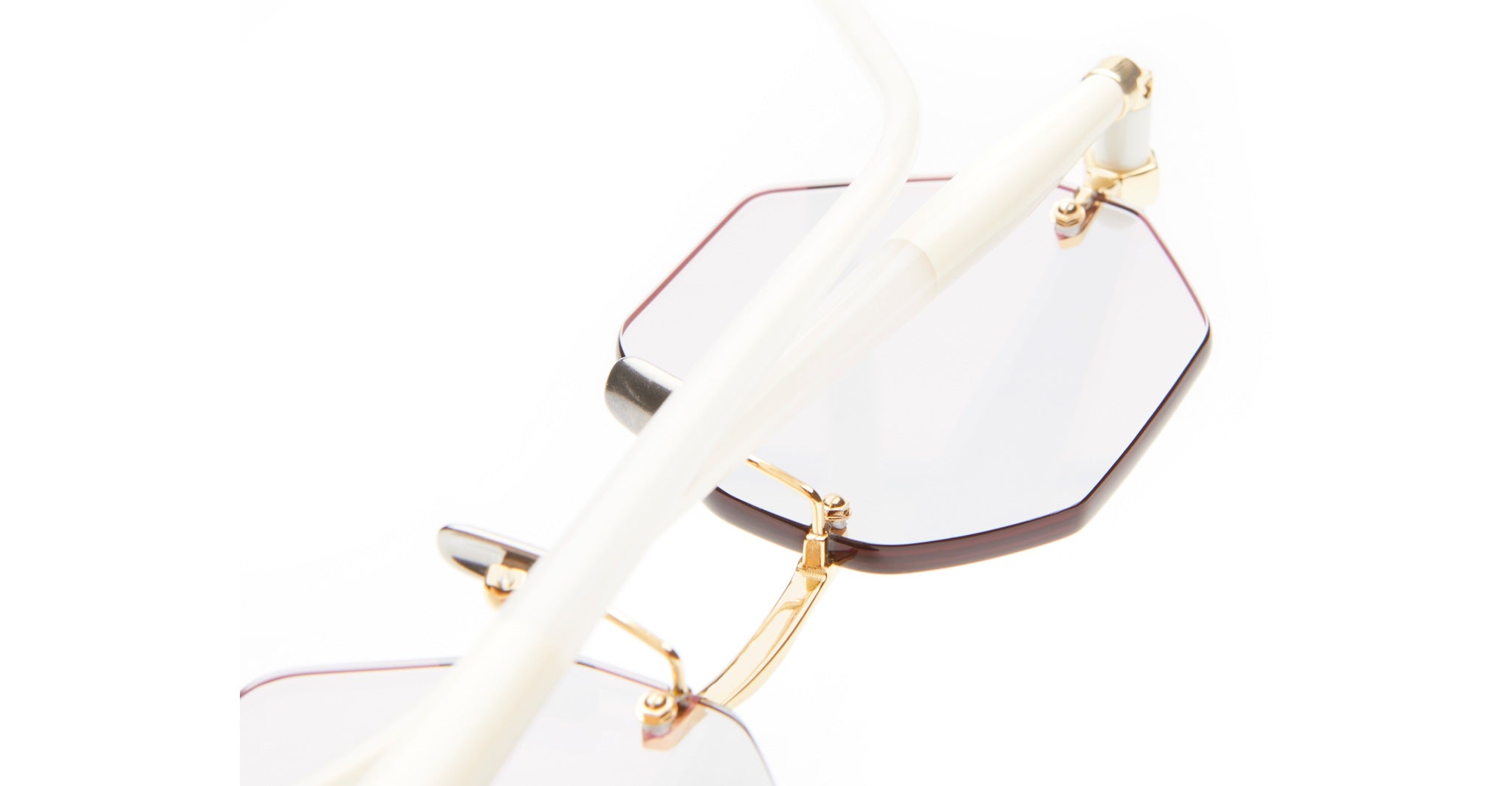 Close-up of the Kuboraum P54 hexagonal eyeglasses featuring gold frames and translucent white arms, positioned at an angle on a white background.