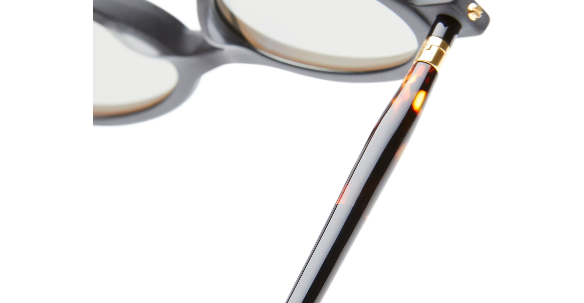 Close-up of Kuboraum P6 eyeglasses, highlighting the black and brown tortoiseshell-patterned arm with a gold hinge, and part of the lenses and frames visible against a white background.