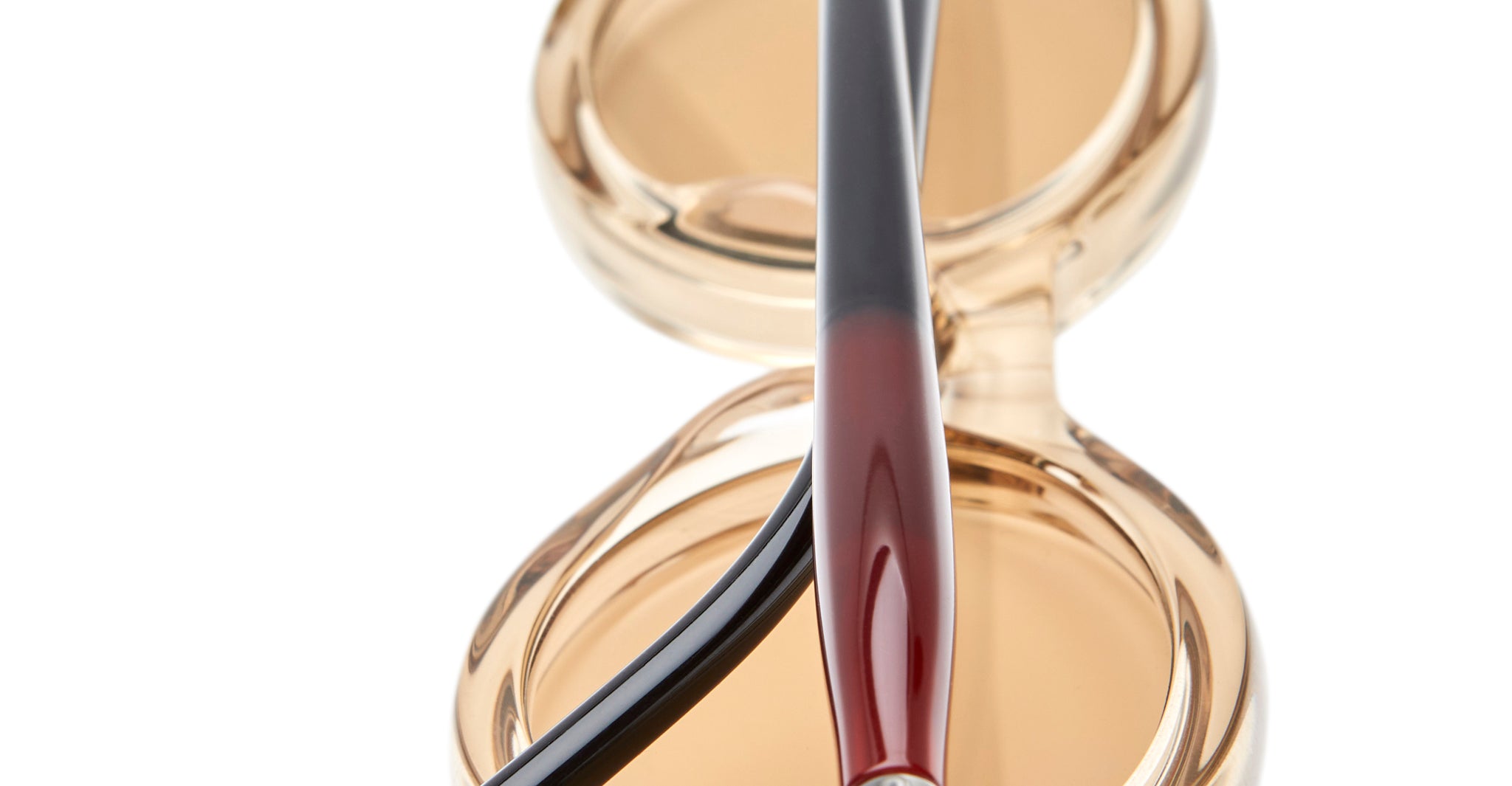 A close-up of the Kuboraum P6 compact powder case with its lid open, placed behind two makeup brushes with black and red handles, all against a white background.