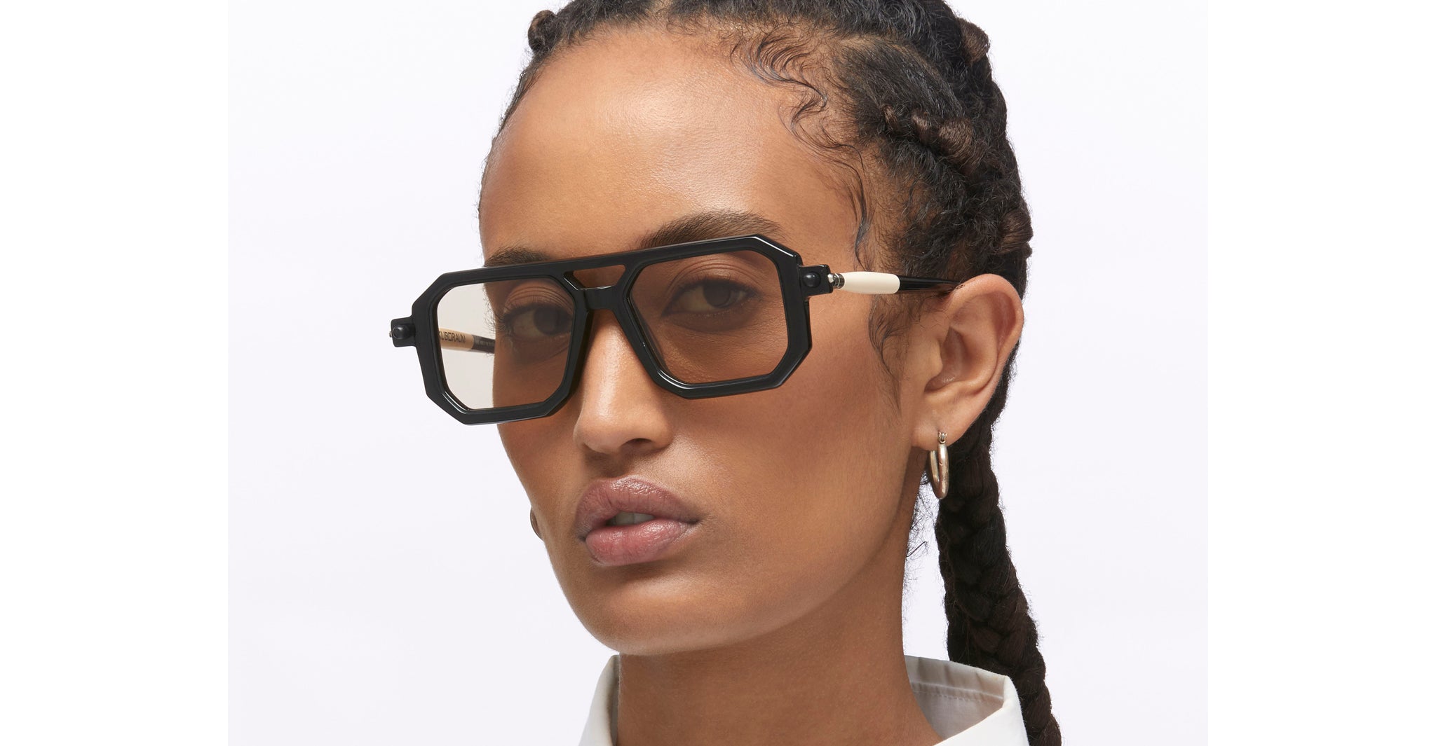 Person with braided hair wearing KUBORAUM P8 black sunglasses and a white shirt, facing the camera.
